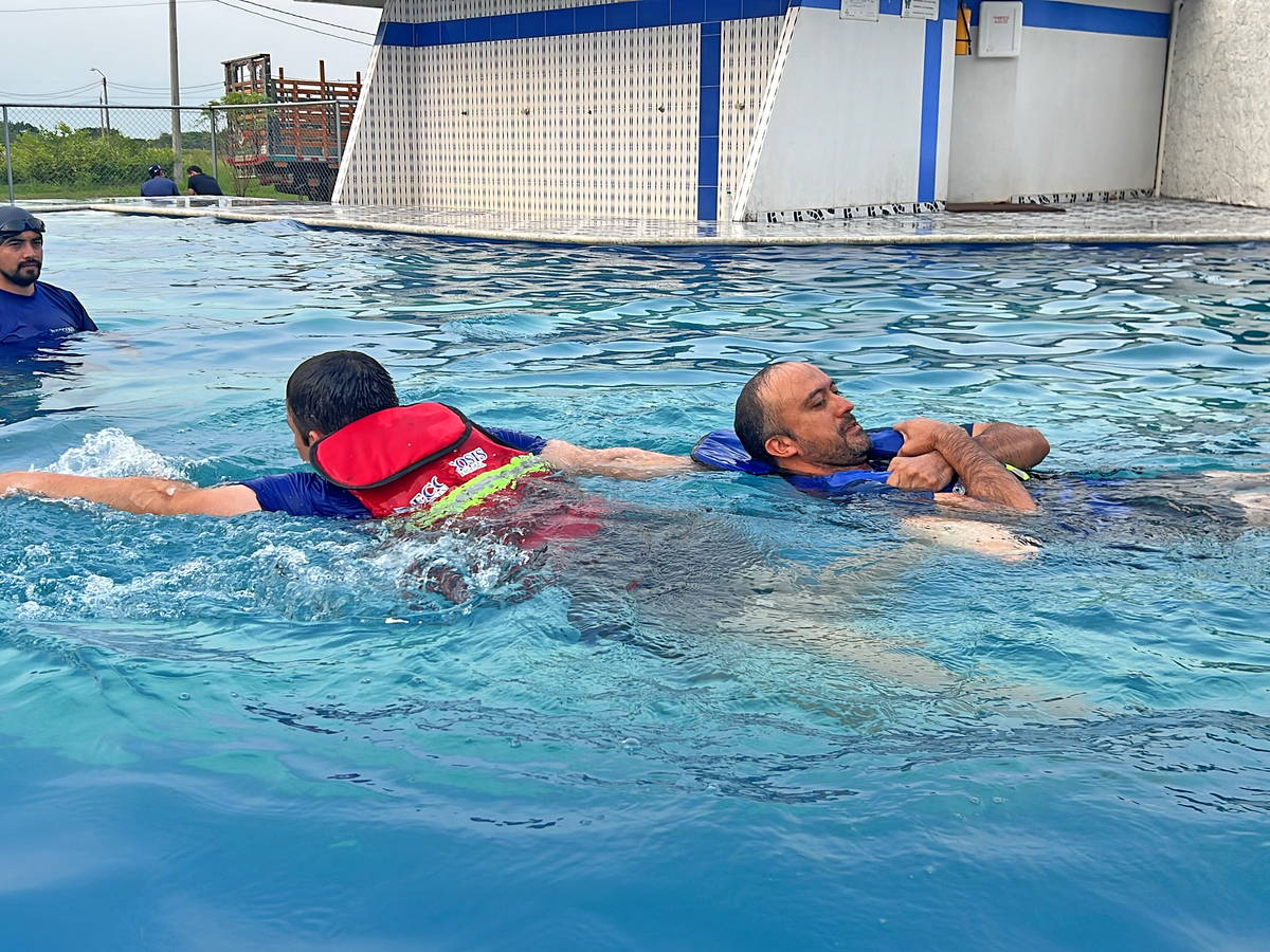 Ejercicio de rescate en piscina: un socorrista con chaleco salvavidas asiste a una persona en el agua.