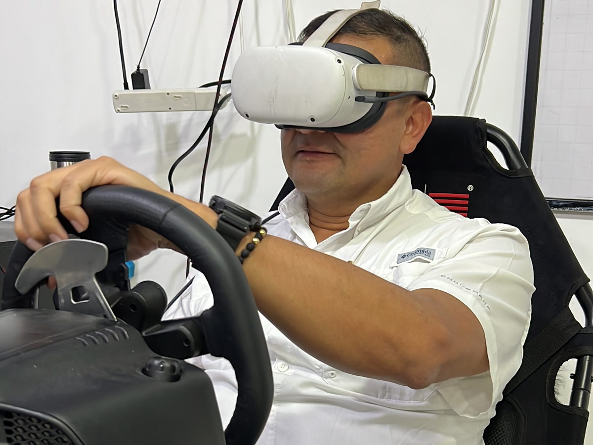 Conductor con visor de realidad virtual sujetando un volante en un puesto de simulación de conducción.