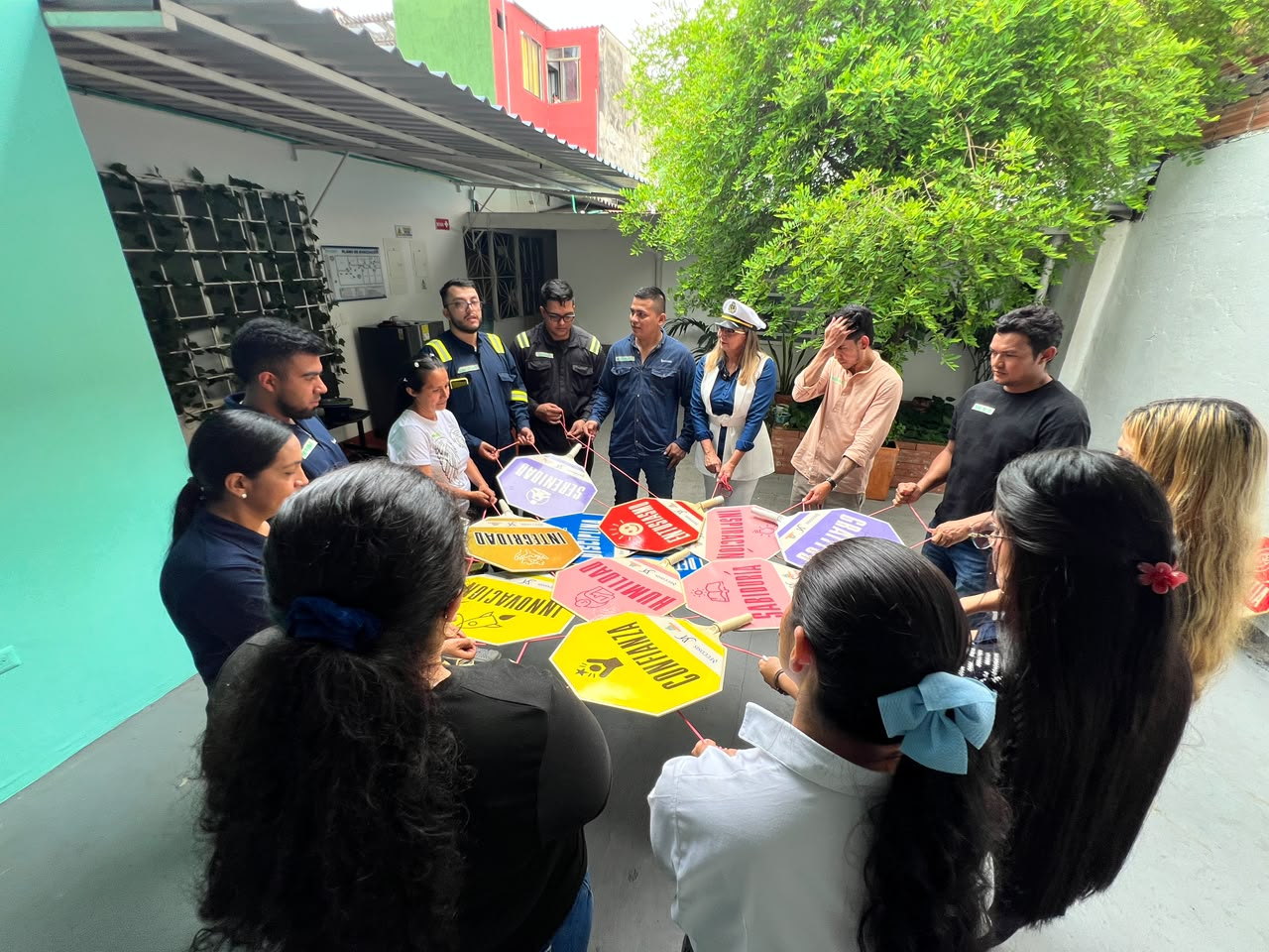 Grupo de trabajadores de pie en círculo durante una jornada lúdico-pedagógica de Eccosis, sosteniendo cuerdas que enlazan señales octogonales con los valores de la organización: confianza, integridad, solidaridad y humildad.