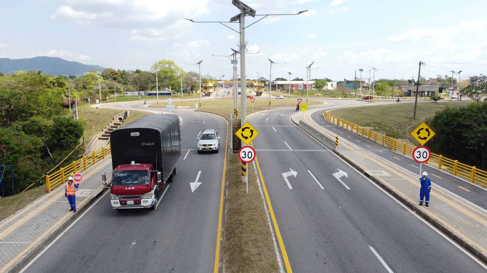 Corredor vial señalizado con demarcación horizontal y señales de velocidad, con auxiliares de tránsito de Eccosis controlando el paso de vehículos de carga.