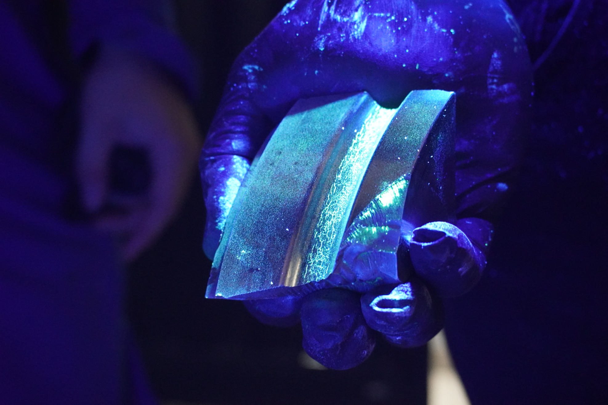 Inspección con partículas fluorescentes bajo luz ultravioleta sobre una pieza metálica, revelando discontinuidades invisibles a simple vista.